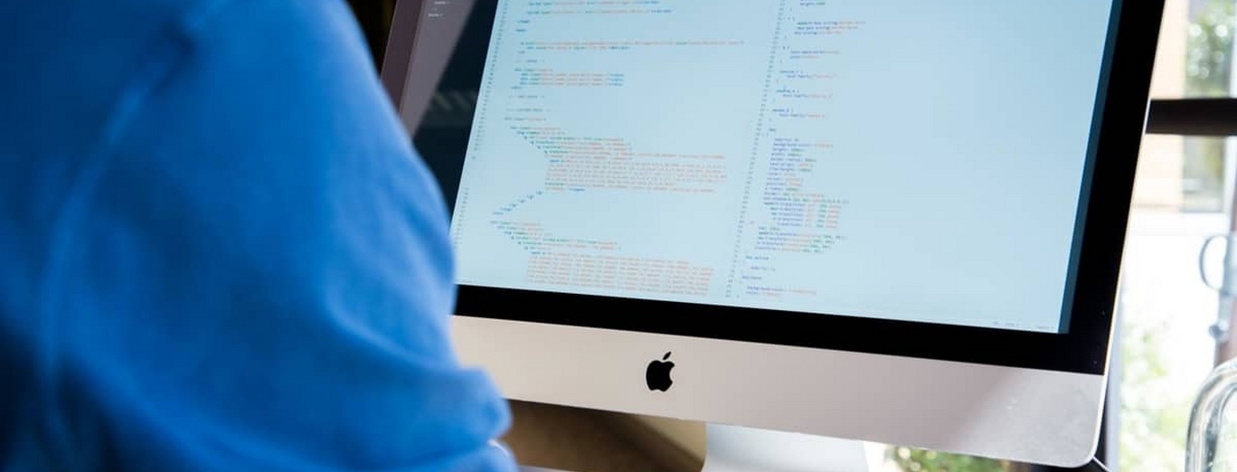 A person working at an iMac with lines of code on its screen