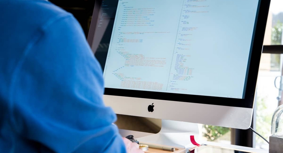 A person working at an iMac with lines of code on its screen